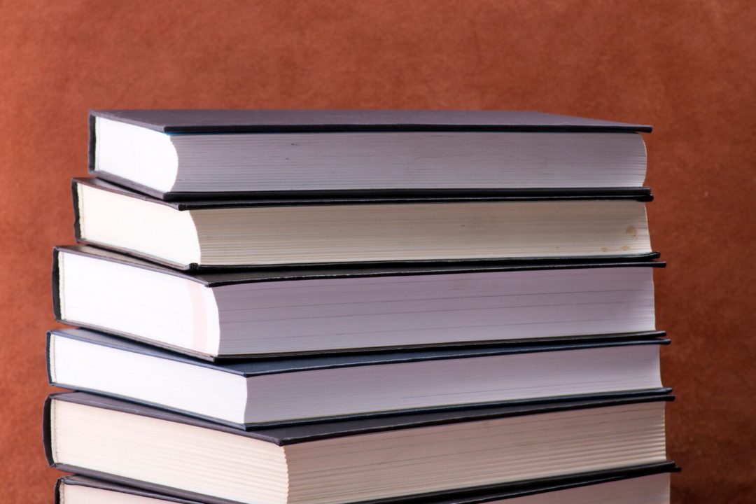 Stacked hardcover books on a red table and brown background creating a classic academic vibe.