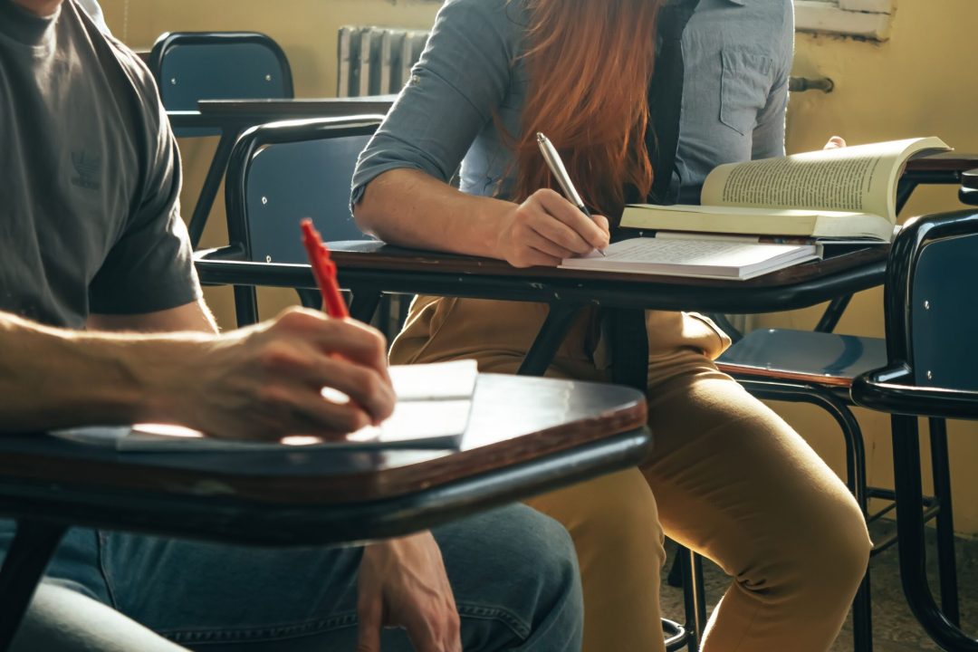 Two students writing notes in a classroom setting, focusing on study and education